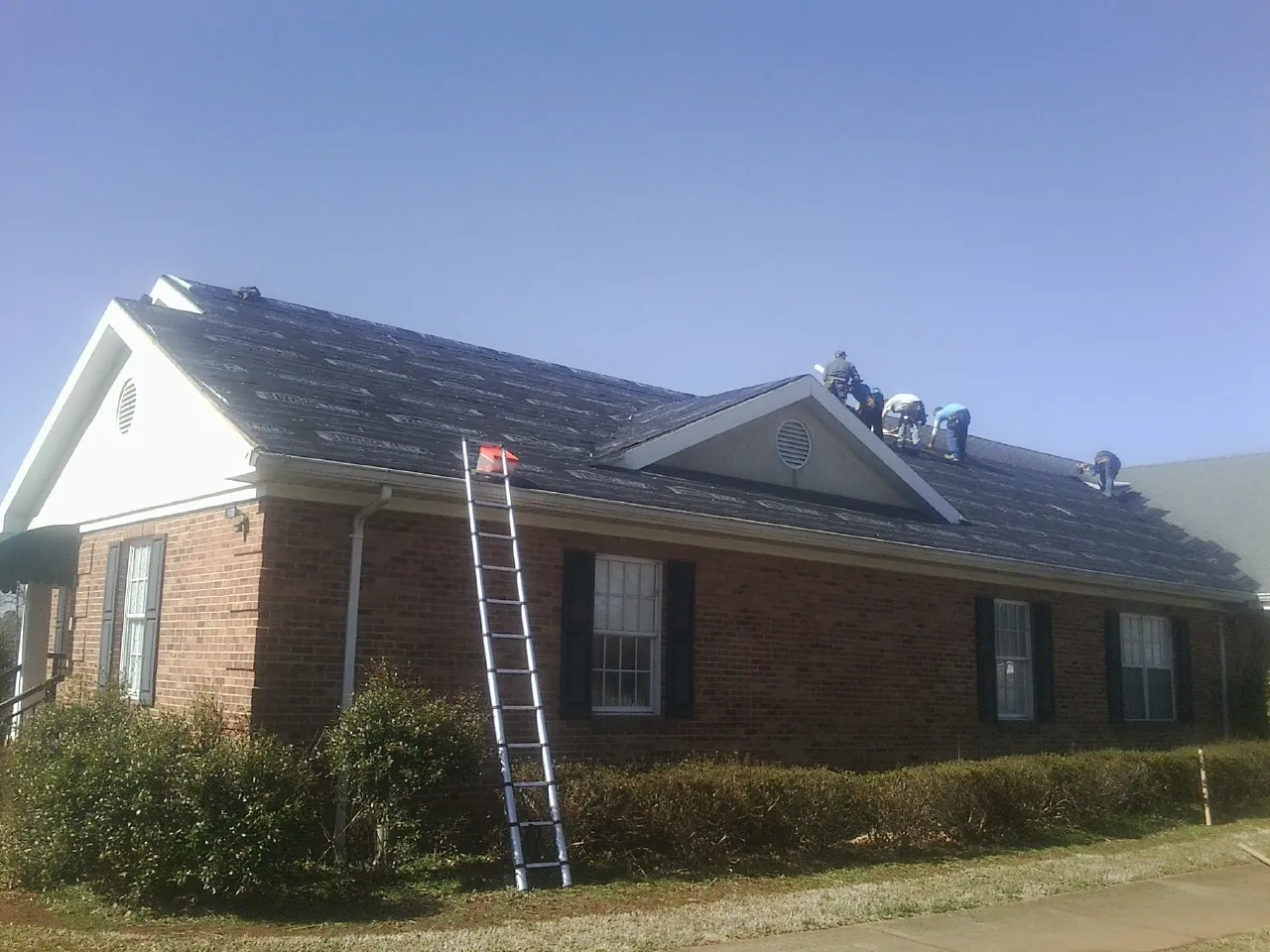 Crew tearing shingles off a brick ranch roof with a ladder set — Metal Roof Repair work by our crew in Mullica Hill