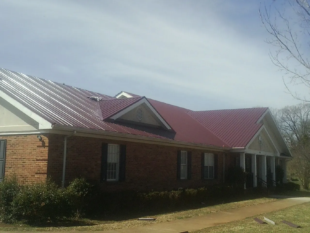Red metal roof with gabled entries on a long brick building, from a Hail Damage Roof Repair job in Mullica Hill