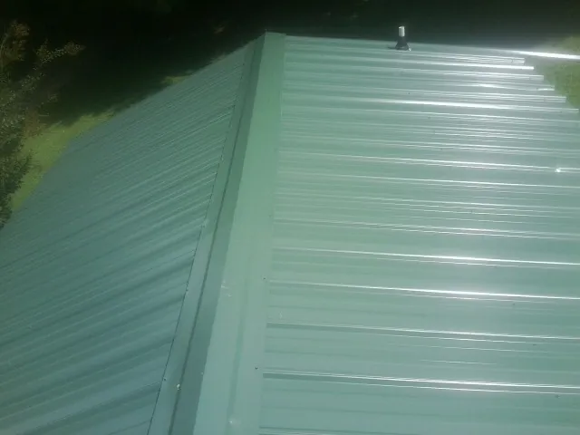 New green metal panels meeting at the ridge of a roof — Flat Roof Repair work by our crew in Mullica Hill