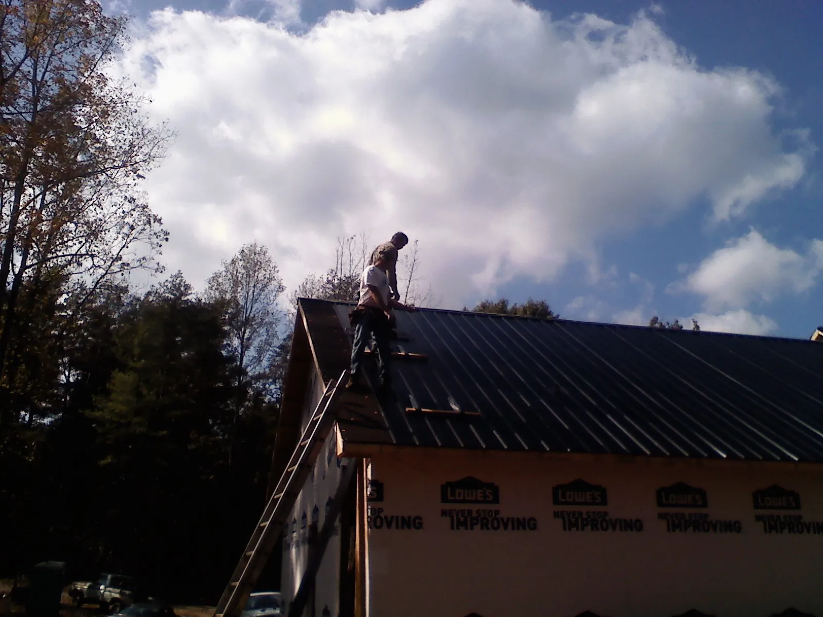 Roofer fastening dark metal panels high against a cloudy sky, from a Roof Inspection job in Mullica Hill