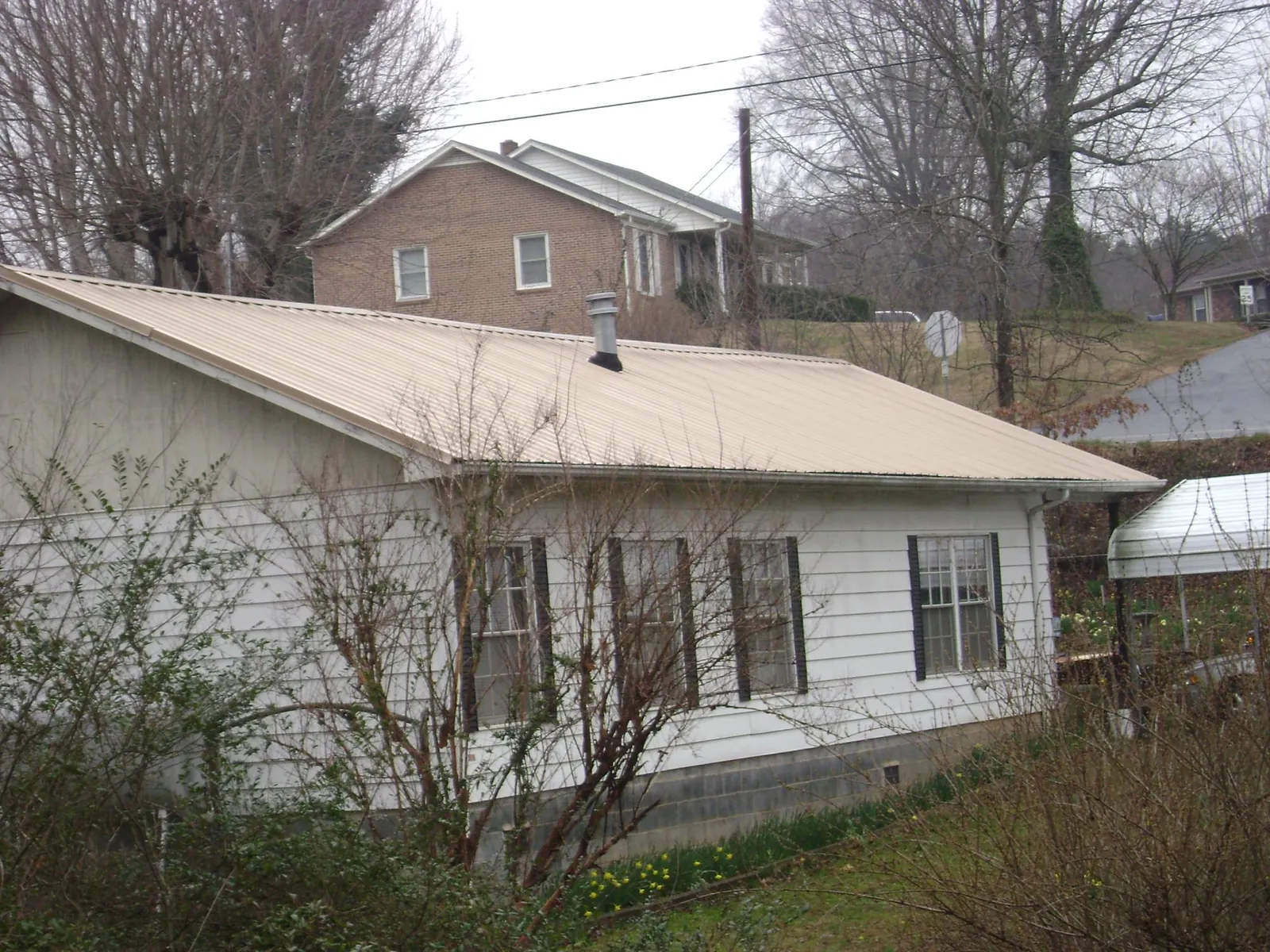 Tan metal roof on a white sided house set into a hillside — Commercial Roofing by Roofing Brothers in Mullica Hill